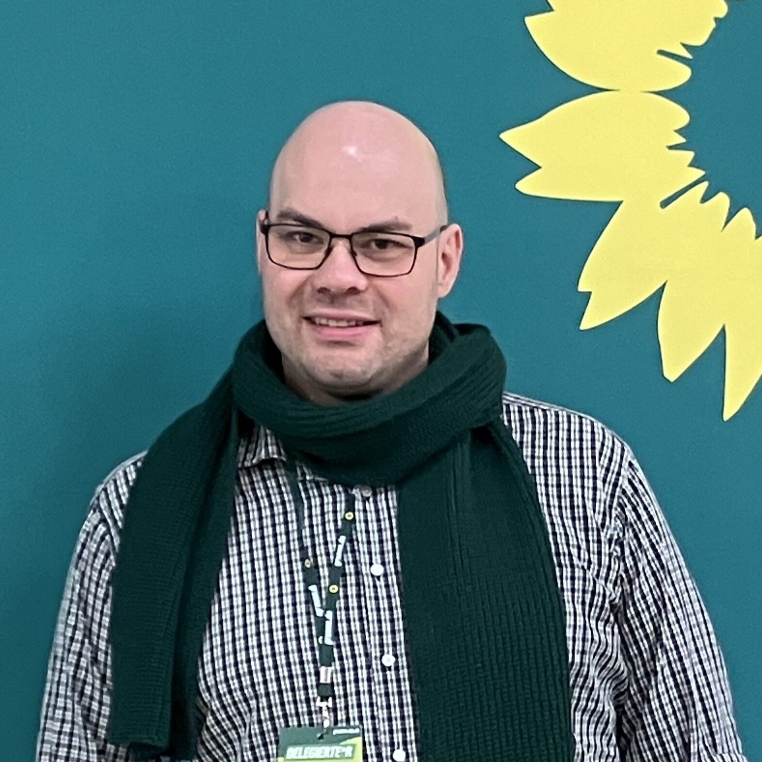 Thomas vor der Grünen Wand, mit Sonnenblumenlogo